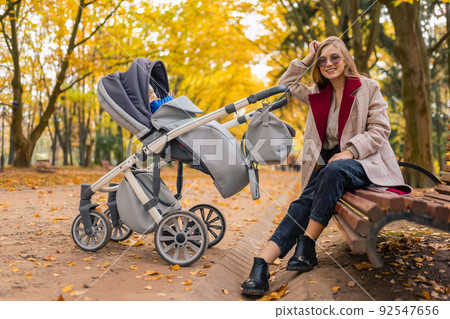 Mother with stroller while walking in the park sat down on bench to rest 92547656