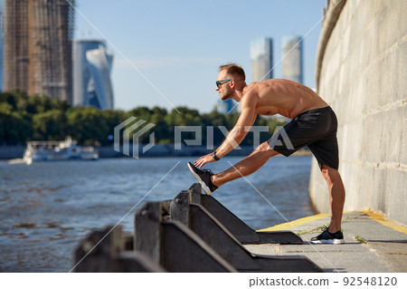 Athletic man running and doing functional workout outdoors - Sportive adult male with sportswear training in a city on the river bank 92548120