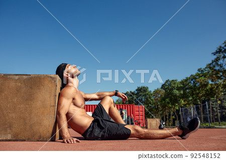 Sporty physically fit man doing step-up exercise on wooden box while doing gym training outdoor. Sporty physically fit man doing step-up exercise on wooden box while doing gym training outdoor. 92548152