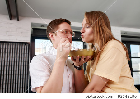 Smiling loving husband feeding wife, young couple enjoying tender moment, romantic date, having fun, eating japanese cuisine, happy family spending free weekend in modern kitchen 92548190