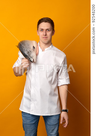 Chef cook holding a big atlantic salmon fish on his shoulder isolated on yellow background Chef cook holding a big atlantic salmon fish on his shoulder isolated on yellow background 92548200