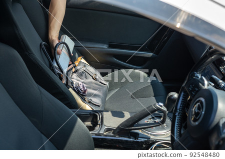 A hand that pulls out a wallet from the passenger seat of a car A hand that pulls out a wallet from the passenger seat of a car 92548480