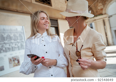 Two stylish female tourists looking at each other outdoors Two stylish female tourists looking at each other outdoors 92548649