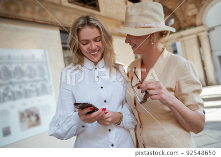 Smiling tourist standing beside a cheerful woman with the cellphone Smiling tourist standing beside a cheerful woman with the cellphone 92548650