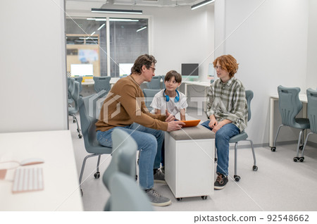 Teacher in eyeglasses explaining something to his students Teacher in eyeglasses explaining something to his students 92548662