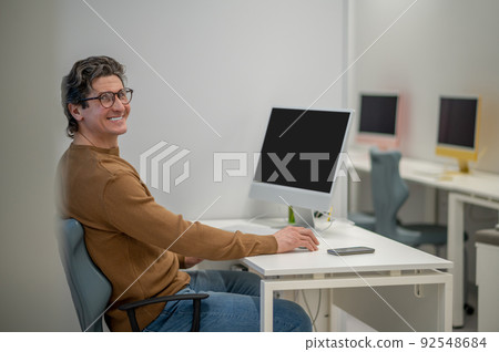 A dark-haired man sitting at the computer and looking involved A dark-haired man sitting at the computer and looking involved 92548684