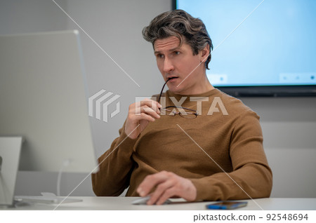 A man sitting at the computer and looking concentrated A man sitting at the computer and looking concentrated 92548694