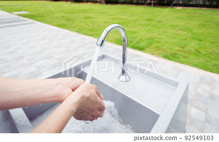 Woman washing hands with tap water under faucet at white sink. Washing hands with tap water at outdoor sink near grass field. Personal hygiene to prevent coronavirus or covid 19. Healthy lifestyle. Woman washing hands with tap water under faucet at white sink. Washing hands with tap water at outdoor sink near grass field. Personal hygiene to prevent coronavirus or covid 19. Healthy lifestyle. 92549103