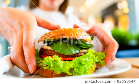 Hamburger vegan healthy vegetarian burger. Salad, avocado, vegetable on veggie sandwich eating cute woman. Tasty vegetarian healthy green food. 92550544