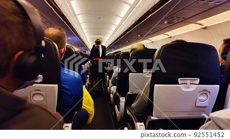 Interior of airplane with passengers on seats and stewardess in uniform walking the aisle 92551452