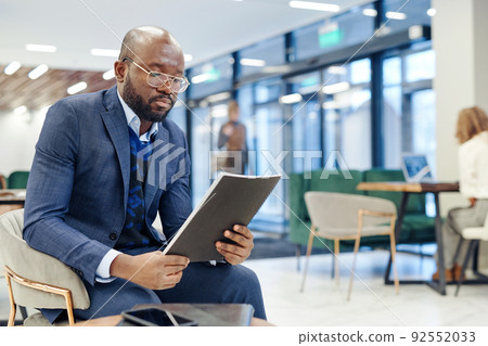 Serious lawyer examining the laws in report while sitting at office hall and waiting for the meeting Serious lawyer examining the laws in report while sitting at office hall and waiting for the meeting 92552033
