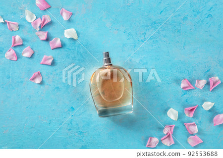Perfume concept. A bottle of rose fragrance, overhead flat lay shot on blue Perfume concept. A bottle of rose fragrance, overhead flat lay shot on blue 92553688