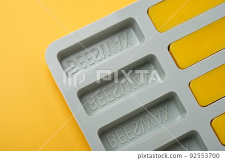 Natural beeswax. Molded bars of beeswax in a silicone mold on a yellow background. Beekeeping products. Copy space. Natural beeswax. Molded bars of beeswax in a silicone mold on a yellow background. Beekeeping products. Copy space. 92553700