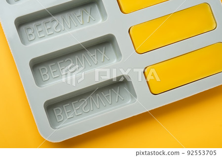 Natural beeswax. Molded bars of beeswax in a silicone mold on a yellow background. Beekeeping products. Copy space. Natural beeswax. Molded bars of beeswax in a silicone mold on a yellow background. Beekeeping products. Copy space. 92553705