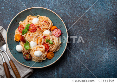 Spaghetti with mozzarella, colourful cherry tomatoes, fresh basil on ceramic plate 92554196