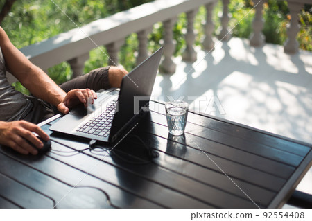 Working at a laptop in the outdoor courtyard - men's hands close-up. Home office, remote work, remote location. Using the keyboard and mouse, relax Working at a laptop in the outdoor courtyard - men's hands close-up. Home office, remote work, remote location. Using the keyboard and mouse, relax 92554408