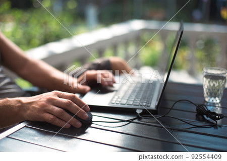 Working at a laptop in the outdoor courtyard - men's hands close-up. Home office, remote work, remote location. Using the keyboard and mouse, relax Working at a laptop in the outdoor courtyard - men's hands close-up. Home office, remote work, remote location. Using the keyboard and mouse, relax 92554409