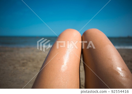 A woman on the beach smears her feet with sunscreen lotion from an orange tube. Skin care, UV protection, sunscreen. Beach holidays A woman on the beach smears her feet with sunscreen lotion from an orange tube. Skin care, UV protection, sunscreen. Beach holidays 92554416