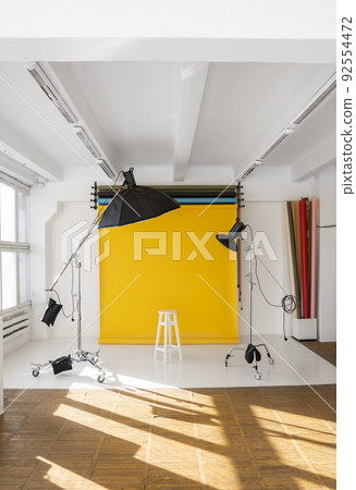Yellow background roll with a white chair and two professional flash on a c-stands. Sunny daylight photo studio interior with set of professional equipment. 92554472