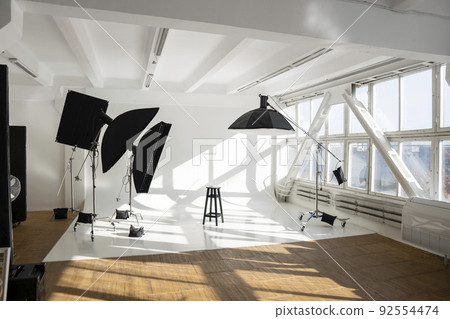 Professional lighting equipment, flashes, c-stands on a cyclorama in modern photo studio with a huge windows. Octabox, stripbox, softbox, buety plate and other stuff for photography. 92554474