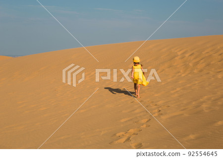A tourist girl in a yellow dress runs along a sandy dune in the desert. Travel, sights of Dagestan, Sarykum dune A tourist girl in a yellow dress runs along a sandy dune in the desert. Travel, sights of Dagestan, Sarykum dune 92554645