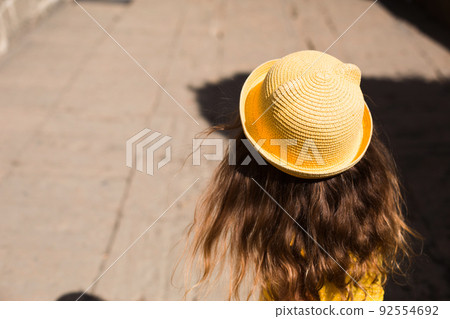 A tourist girl in a yellow hat and sundress walks along the street of the old town made of stone with a fortress. Sightseeing tour. The child got lost, searching for parents 92554692
