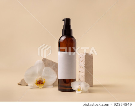 Dark glass cosmetic bottle near white orchid flowers and stones on light yellow, close up, Mockup 92554849