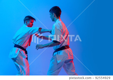 Studio shot of sports training of two karatedo fighters in doboks isolated on blue background in neon. Concept of combat sport, challenges, skills 92554929