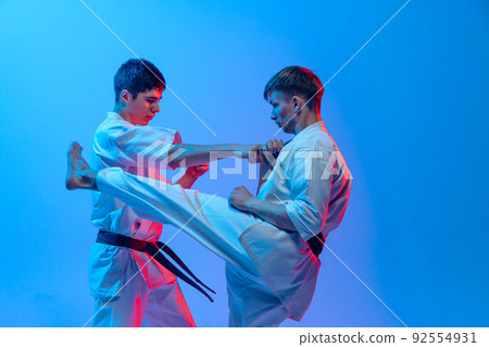 Studio shot of sports training of two karatedo fighters in doboks isolated on blue background in neon. Concept of combat sport, challenges, skills 92554931