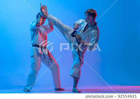 Studio shot of sports training of two karatedo fighters in doboks isolated on blue background in neon. Concept of combat sport, challenges, skills 92554935