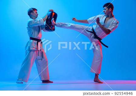 Studio shot of sports training of two karatedo fighters in doboks isolated on blue background in neon. Concept of combat sport, challenges, skills 92554946