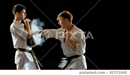 Dynamic portrait of male karate-do fighters in sports uniform training together isolated on black background. Concept of sport, education, skills, martial arts, health 92555040