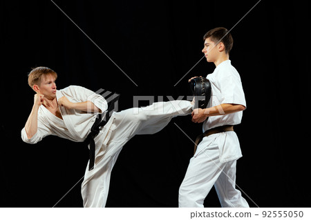 Dynamic portrait of male karate-do fighters in sports uniform training together isolated on black background. Concept of sport, education, skills, martial arts, health 92555050