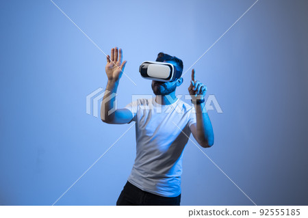 Serious millennial male student in white t-shirt and vr glasses moves his hands manipulating gestures in virtual reality world. 3d technology, virtual reality and entertainment concept. 92555185