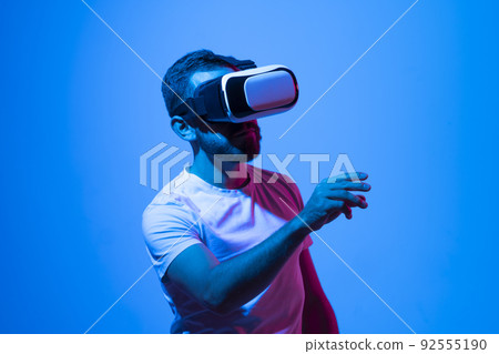 Young man close-up portrait wearing VR headset and speaking with a friends in metaverse while playing a games. Young man close-up portrait wearing VR headset and speaking with a friends in metaverse while playing a games. 92555190