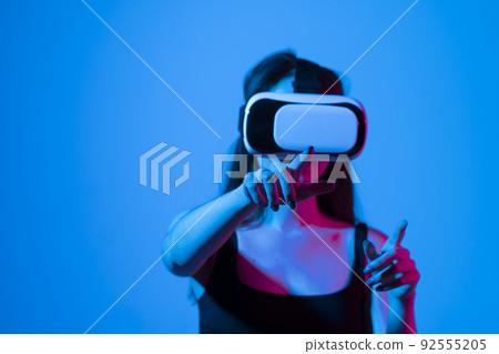 Woman using VR virtual reality glasses headset pointing at objects in metaverse. Virtual reality metaverse. Woman using VR virtual reality glasses headset pointing at objects in metaverse. Virtual reality metaverse. 92555205