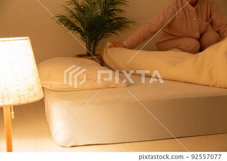 A middle-aged woman wearing pajamas and preparing a futon 92557077