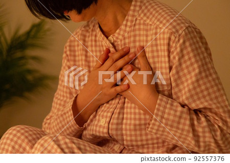 Middle-aged woman in pajamas suffering from chest pain Middle-aged woman in pajamas suffering from chest pain 92557376