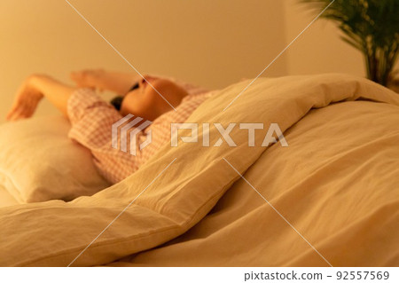 A middle-aged woman wearing pajamas and stretching with a futon A middle-aged woman wearing pajamas and stretching with a futon 92557569