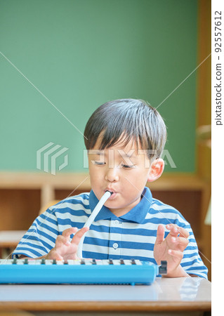 Elementary school boy playing keyboard harmonica in the classroom 92557612
