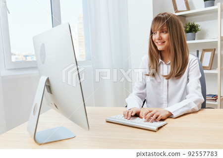 Happy smiling adorable blonde businesswoman worker freelancer look at screen typing answer for clients in light modern office. Cheerful employee work on computer online in support service. Copy space 92557783