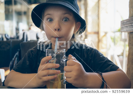 Little girl with a mug of lemonade in a cafe. High quality photo 92559639