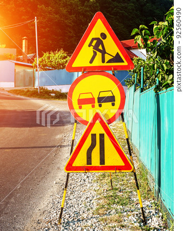 Roadwork signs on the side of the road. Yellow-red warning signs on the gravel side of a rural road. Road works in progress 92560490