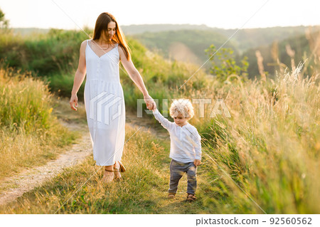 Mom and son walk holding hands in the summer field Mom and son walk holding hands in the summer field 92560562