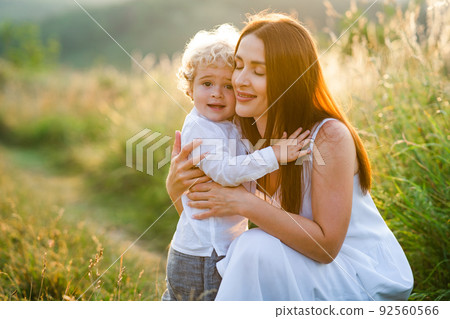 Loving mother hugs her son while walking in a picturesque field. 92560566