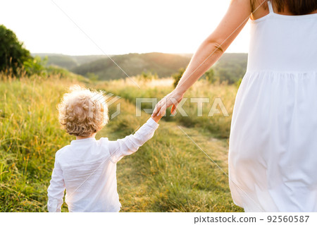 Boy with curly hair walks with his mother by the hand in a summer field Boy with curly hair walks with his mother by the hand in a summer field 92560587