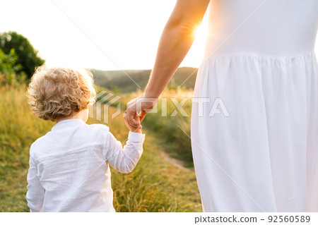 Back view of mom and son walking in the field at sunset Back view of mom and son walking in the field at sunset 92560589