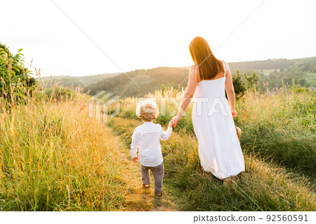 Mother and son are walking holding hand in a beautiful hilly area at sunset Mother and son are walking holding hand in a beautiful hilly area at sunset 92560591