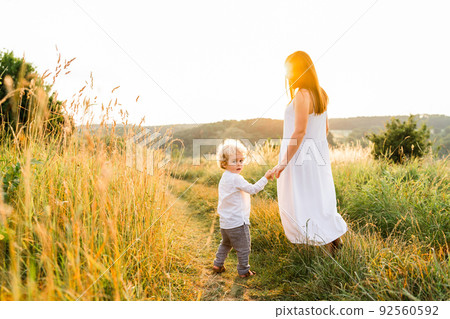 Mother and son walk along the field path, looking back and looking at the camera Mother and son walk along the field path, looking back and looking at the camera 92560592