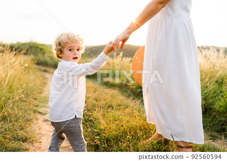 Handsome boy with curly hair walks with his mother in nature holding her hand. Handsome boy with curly hair walks with his mother in nature holding her hand. 92560594